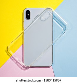 Clear IPhone Case Mock Up. Smart Phone On A Background Of Pink, Yellow And Blue Paper, Silicone Transparent Case Back View Mockup