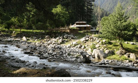 A clear mountain stream flows past a rustic house in a serene forested area of Kashmir, Neelum valley - Powered by Shutterstock