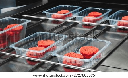 Clear, open plastic boxes containing red cookies are being processed. Several trays are on a conveyor belt, ready for further packaging and transportation.