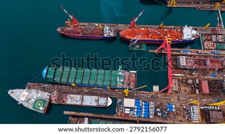 Clear overhead drone shot capturing massive shipyard drydocks with industrial cranes and various commercial vessels undergoing maintenance and repair works.