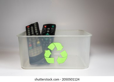 Clear Plastic Box With The Recycling Symbol Containing Two Old Tv Remote Controls On A White Background