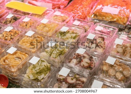 Clear plastic containers filled with different kinds of pre-packaged raw marinated seafood and appetisers selling in the supermarket.