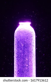 Clear Plastic Water Bottle Filled With Water, Placed On A Black Background, Turn On The Purple Light And Spray Water Down, The Findings In A Beautiful Spray. Concept Images For Product Advertising