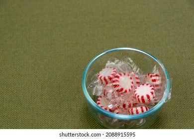 Clear Plastic Wrapped Red And White Peppermint Hard Candies In A Small Clear Glass Bowl On A Green Tablecloth. Holiday White And Red Peppermint Hard Candy Discs In A Small Bowl On A Green Tablecloth.