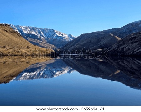 Clear reflections on the Snake River near Oxbow, Oregon, with snow-dusted mountains and steep canyon walls under a cloudless sky.