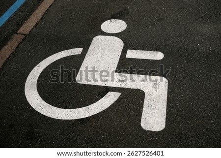 A clear representation of an accessible parking symbol on a worn asphalt surface outdoors.
