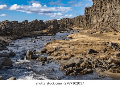 A clear river winds through a rugged volcanic canyon surrounded by ancient rock formations. The dramatic terrain and expansive sky create a powerful wilderness scene ideal for travel, geology, and nature themes.