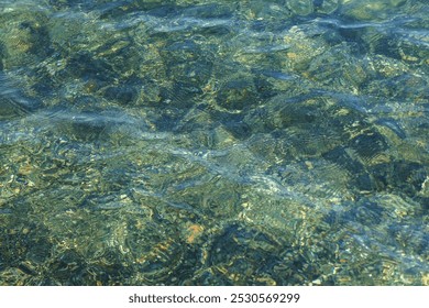 Clear, shallow water gently flows over smooth rocks, with sun reflecting off the surface. - Powered by Shutterstock