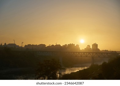 Clear sky over the river and railway bridge during sunrise. Smog over the city because of a factory with smoking pipes. Protection of the environment from harmful emissions