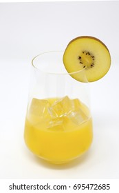 A Clear, Stemless Wine Glass With Organic Orange Juice And Ice.  A Slice Of Sun Gold Kiwifruit Is On The Rim Of The Glass 