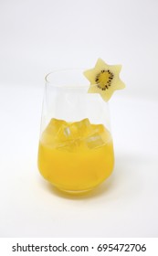 A Clear, Stemless Wine Glass With Organic Orange Juice And Ice.  A Slice Of Sun Gold Kiwifruit In The Shape Of A Star Is On The Rim Of The Glass