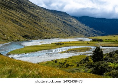 A clear stream flowing through a mountain valley, surrounded by green meadows and rocky terrain.