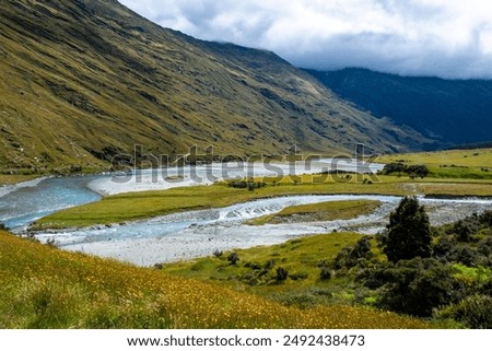 A clear stream flowing through a mountain valley, surrounded by green meadows and rocky terrain.