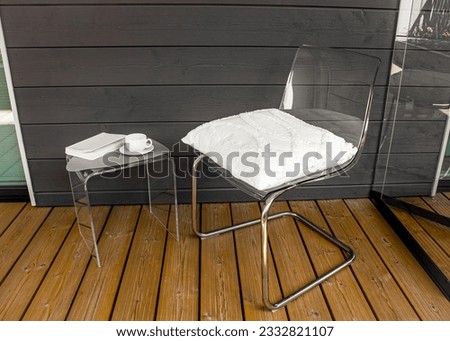 Clear transparent modern acrylic furniture in home. Chair with pillow, side table with tea cup and book. Alternative furniture material concept.