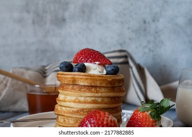 Clear View Of Stack Of Pancakes With Honey Stick, Strawberry, Blue Berry And Whip Cream On Top In Plate, Delicious Dessert With Milk For Breakfast.