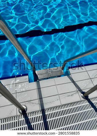A clear view of a swimming pool with steps leading into it, featuring blue water reflections and tiled edges.