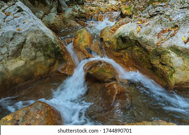 Clear Water Runs Through The Grey Stones, Background. The Water Rolls Over The Stone Rapids, Forming Breakers, Whirlpools And Foam. The Concept Of Freshness And Eternal Movement.