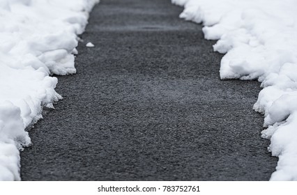 Cleared Snow Path Along A Dark Tarmac Surface.