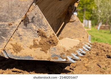 Clearing and leveling a private land plot. Yellow excavator driving earth in a wide bucket