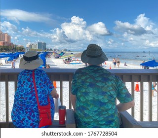 Clearwater Beach, Florida - June 20, 2020: Older Couple Sitting On A Bench Looking At The Beach