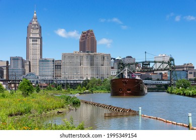 Cleveland, Ohio June 22, 2021:  An articulated tugboat and barge laden with aggregate material for a local industry moves up the Cuyahoga River with the downtown Cleveland skyline in the background