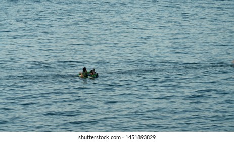 Cleveland, Ohio/USA - July 4, 2019: Solo Inner Tube In Body Of Water With Group Of People. Distant View Of Recreational Holiday Goers On Lake Erie Having Fun Being Pulled By Fishing Boat.