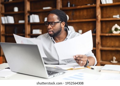 Clever and concentrated African-American guy is doing paperwork, a man looking through workpaper sitting at the desk with a laptop in office, a man checking report, collate data - Shutterstock ID 1952564308