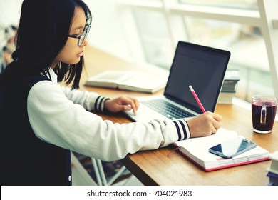 Clever International Student Concentrated On Writing In Notebook Preparing Homework In Coworking Space, Young Pupil In Eyewear Making Researches Via Laptop Analyzing Information From Network 