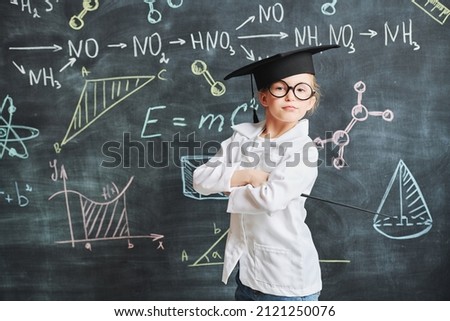 Clever kids. Portrait of a cute smart little girl in white shirt and glasses standing at the blackboard with chemical formulas with teacher's pointer in her hand. Education. 