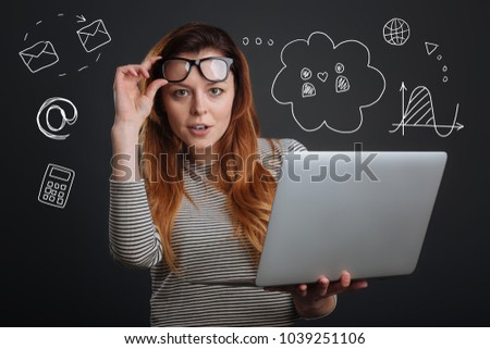 Clever woman. Calm smart young employee standing with her fingers touching the glasses and looking confident while holding a convenient laptop and thinking about her work