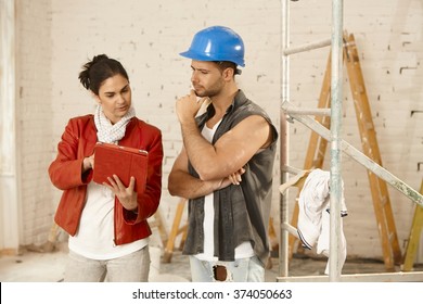 Client And Contractor Talking At Renovation Site, Using Tablet Computer.