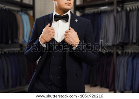 client is elegant guy trying on a suit in a mirror shop. In the background classic suits and jackets