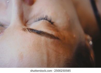 Client is having an eyebrow tint applied during an eyebrow correction procedure by a beautician. The client is lying on a table with their eyes closed - Powered by Shutterstock