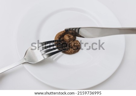 The client holds a stainless fork and knife and cuts artificial plastic feces.Expired product.The concept of an inept cook, fake news, a crappy restaurant, bad food, a taste of shit. Bad smelling joke