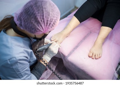 A client at a reception with a pedicure master lies on the couch. The pedicurist works with the toenails by polishing them.