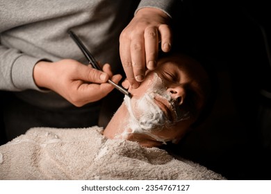 Client relaxing while sitting in barber's chair and getting shave by male barber. Self care theme - Powered by Shutterstock