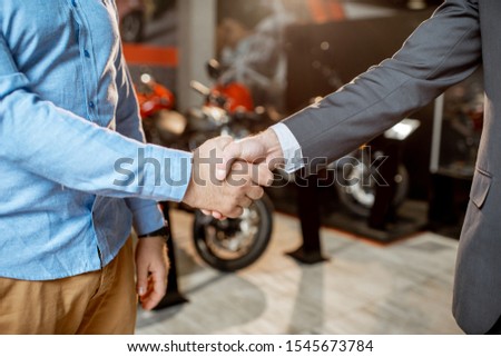 Client shaking hands with a salesman having deal in the showroom with sports motorcycles, close-up