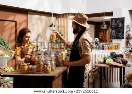 Client shopping for pantry staples in environmentally conscious zero waste store, being assisted with advice by trader. Merchant showing woman ecological nonpolluting products