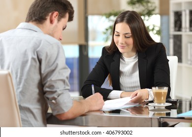 Client signing a document in an office with a businesswoman looking the contract