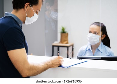 Client Signing Paper At Reception Desk In Face Mask