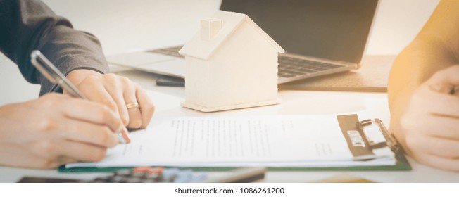 Client Signs Document Regarding Real Estate Activity Next To Lawyer Or Real Estate Agent Sitting At Office Desk. Business Concept Of Selling And Buying Real Estate.