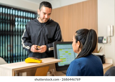 Client standing at a reception desk, interacting with a female receptionist, preparing for an appointment or making a payment
