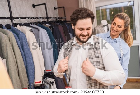 Client trying on a checkered jacket with tailor assisting in a boutique