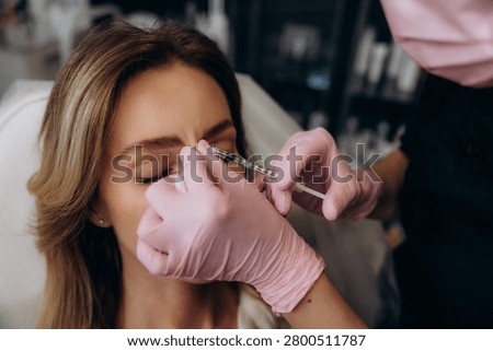 Client undergoing anti-aging aesthetic procedure, a cosmetologist injecting a solution into her forehead to reduce wrinkles