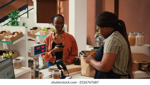 Client using nfc payment at pos to buy eco products, visiting local farmers market to restock pantry essentials. Vegan woman paying with mobile phone at checkout, nonpolluting goods. Handheld shot. - Powered by Shutterstock