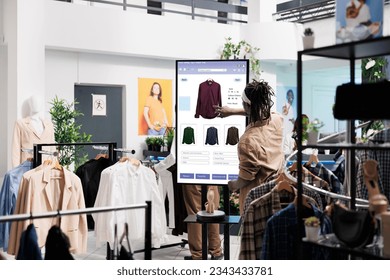 Client using touch screen board in trendy clothing store, shopping for fashion collection items in shop. Young buyer buying clothes on interactive monitor, self ordering concept. - Shutterstock ID 2343433781