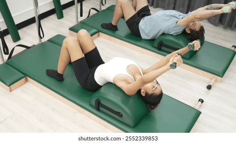 Clients performing arm and leg stretches using small weights on Pilates arc barrel equipment. Couple of trainer make supine arm and leg reaches with weight for improving core and stability. Habituate. - Powered by Shutterstock