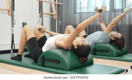 Clients performing arm and leg stretches using small weights on Pilates arc barrel equipment. Couple of trainer make supine arm and leg reaches with weight for improving core and stability. Habituate. - Powered by Shutterstock