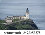 From the cliffs above looking down on the white building of Neist Point Lighthouse perched on a cliff above the sea on the Isle of Skye in Scotland.