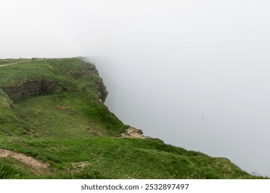 Cliffs of Moher in County Clare, Ireland, reveals a grassy cliff edge fading into the dense mist. The soft light and overcast conditions create a peaceful yet mysterious atmosphere - Powered by Shutterstock